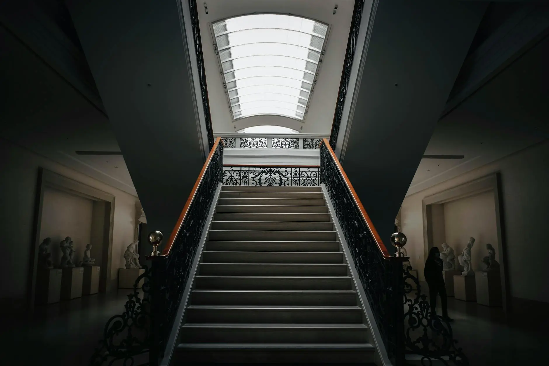 A dimly lit museum hallway with stairs and sculptures