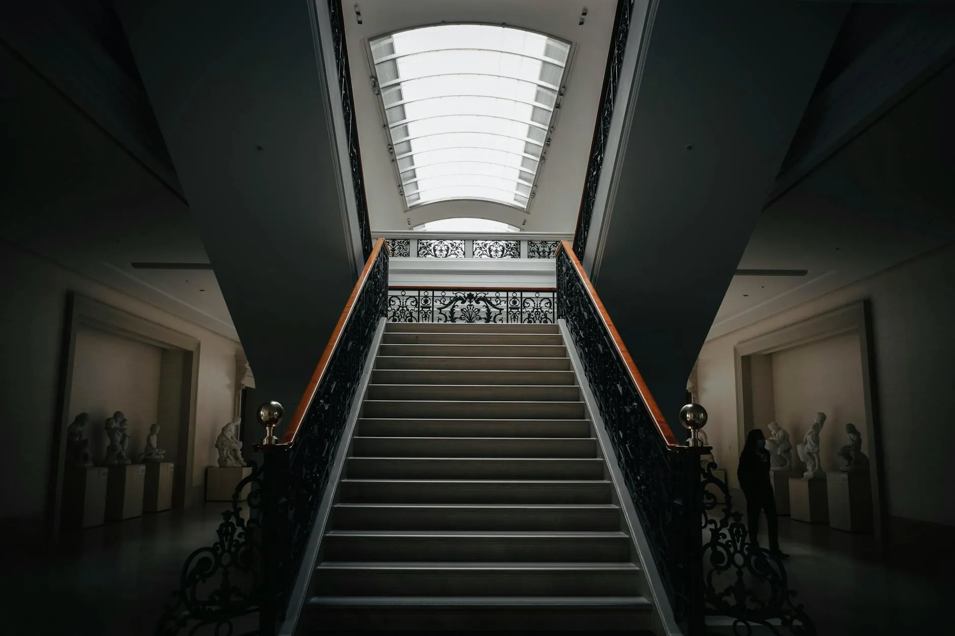 A dimly lit museum hallway with stairs and sculptures