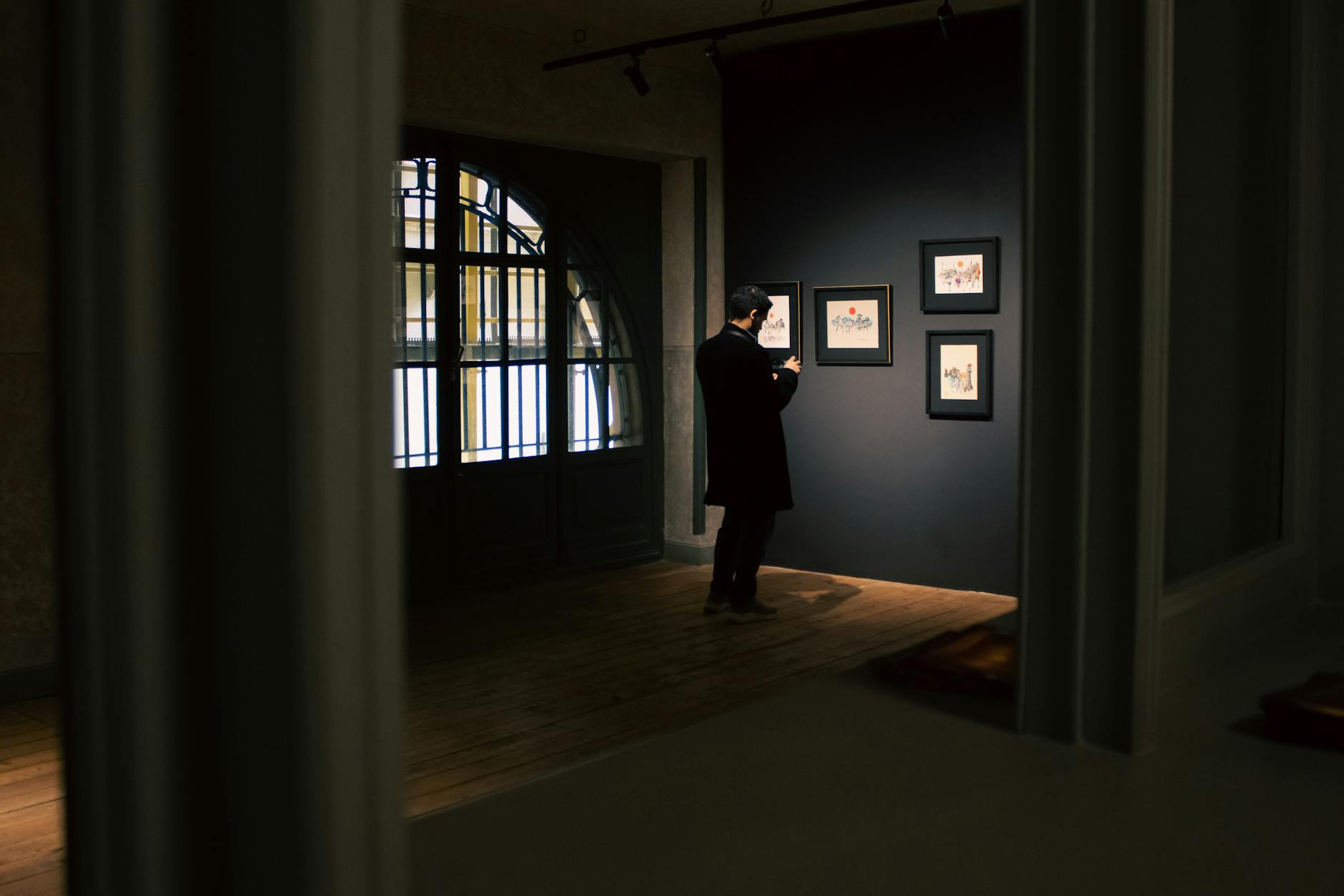 Man studying framed artwork in a dimly lit gallery